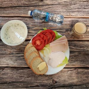 Zdjęcie przedstawia Dietę podstawową: Kawa zbożowa z mlekiem Owsianka budyniowa z bananem i jabłkiem z posypką chia Chleb mieszany pszenno-żytni Masło extra Szynka Drobiowa, parzona, z dodatkiem białka wieprzowego Pomidor Woda mineralna Sałata lodowa Twarożek truskawkowy